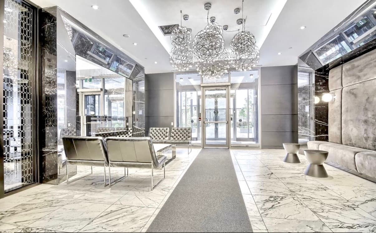 Modern luxury lobby featuring marble floors, metallic chairs, and large spherical wire chandeliers.