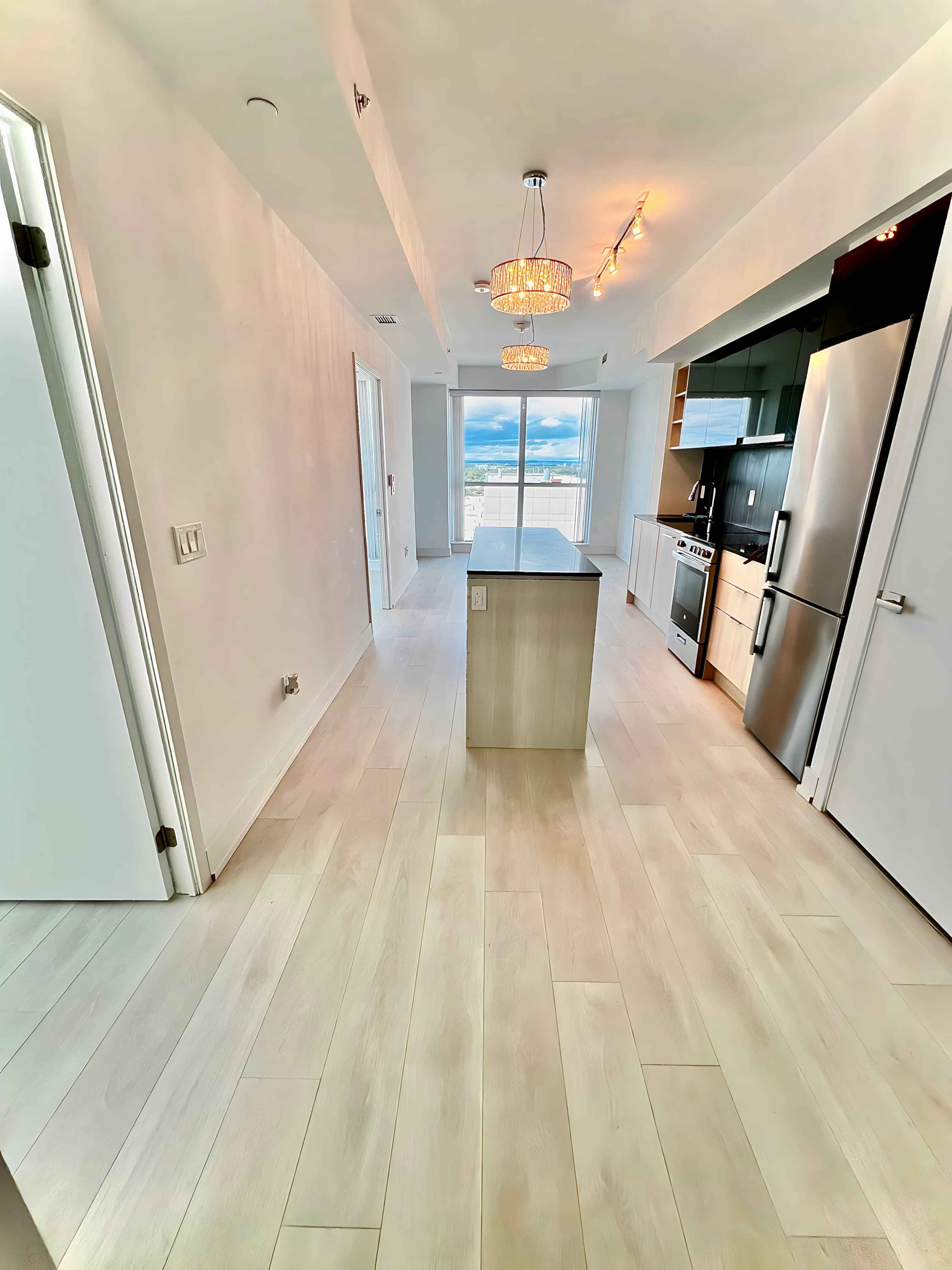 Modern kitchen featuring light wood floors, a central island, stainless steel appliances, and city views.