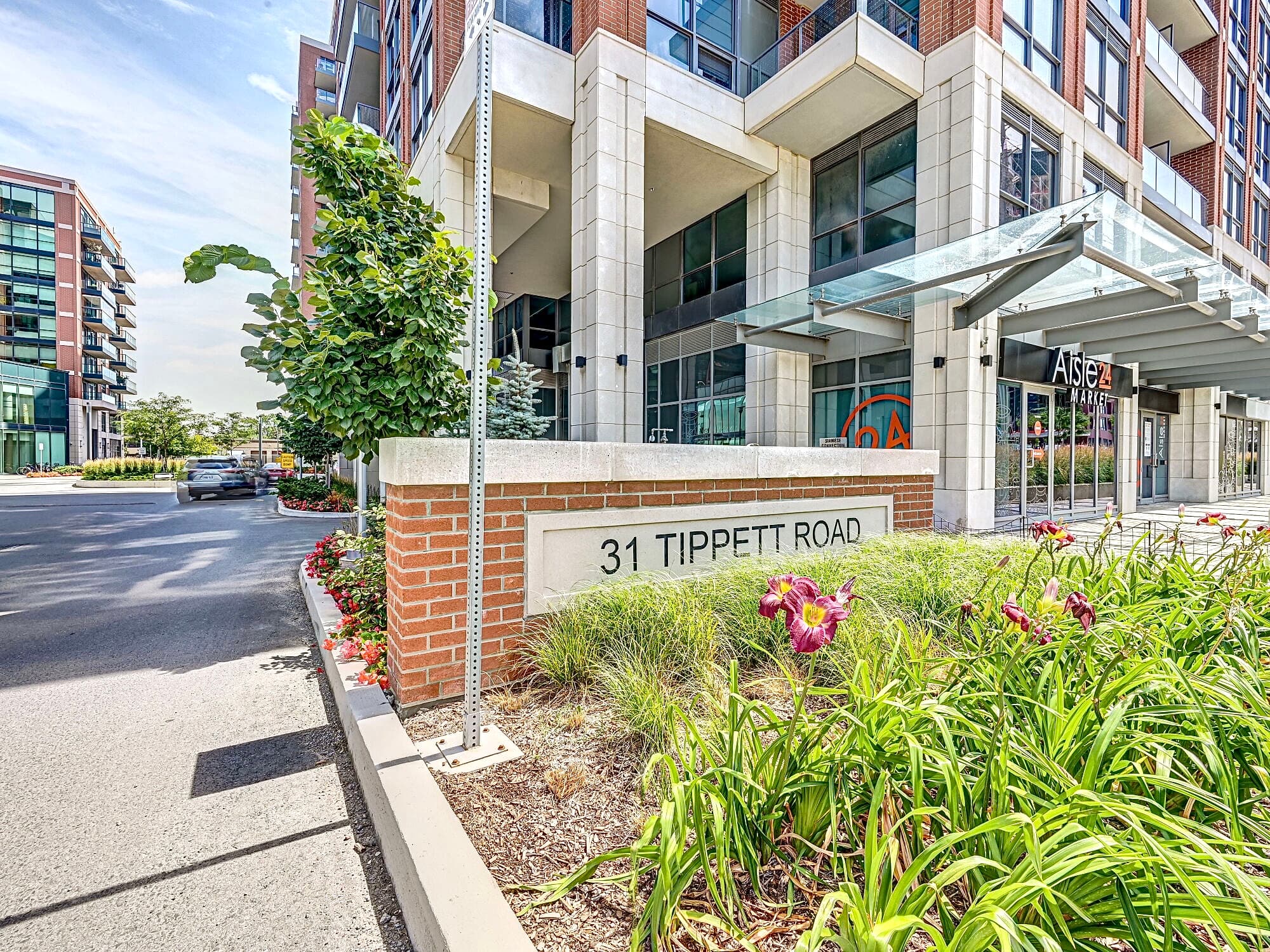 Brick sign for 31 Tippett Road featuring purple flowers and a modern apartment building.