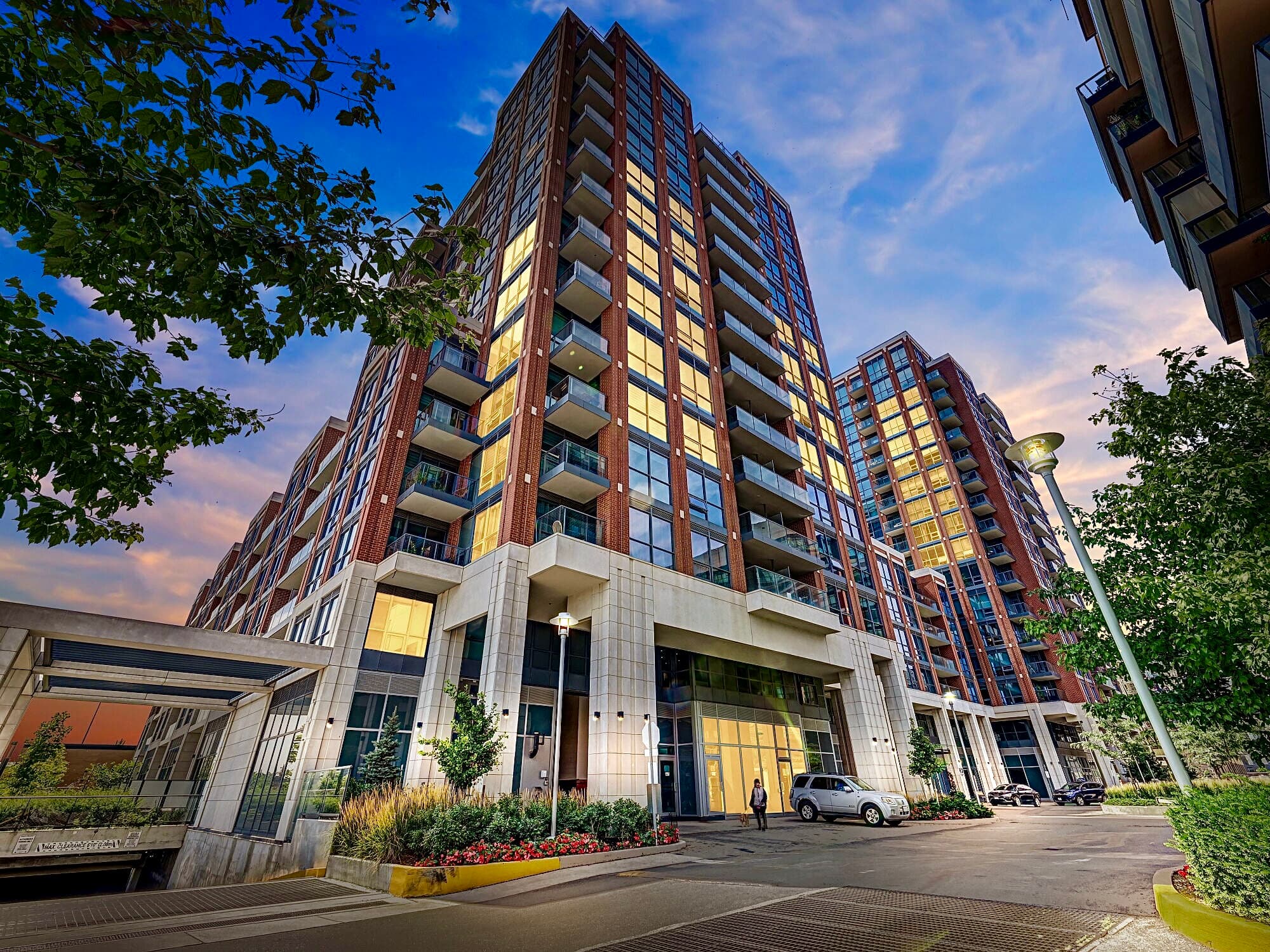 Modern high-rise apartment building with glowing windows and balconies under a colorful twilight sky.