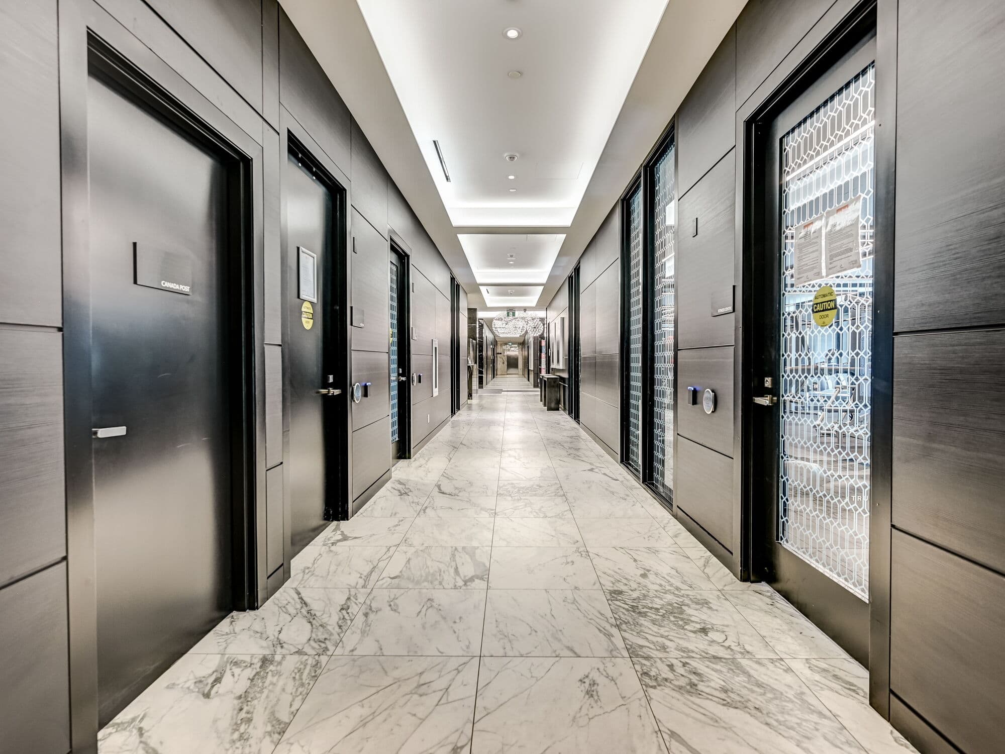 Long, modern hallway with white marble floors, dark paneled walls, and bright recessed ceiling lights.