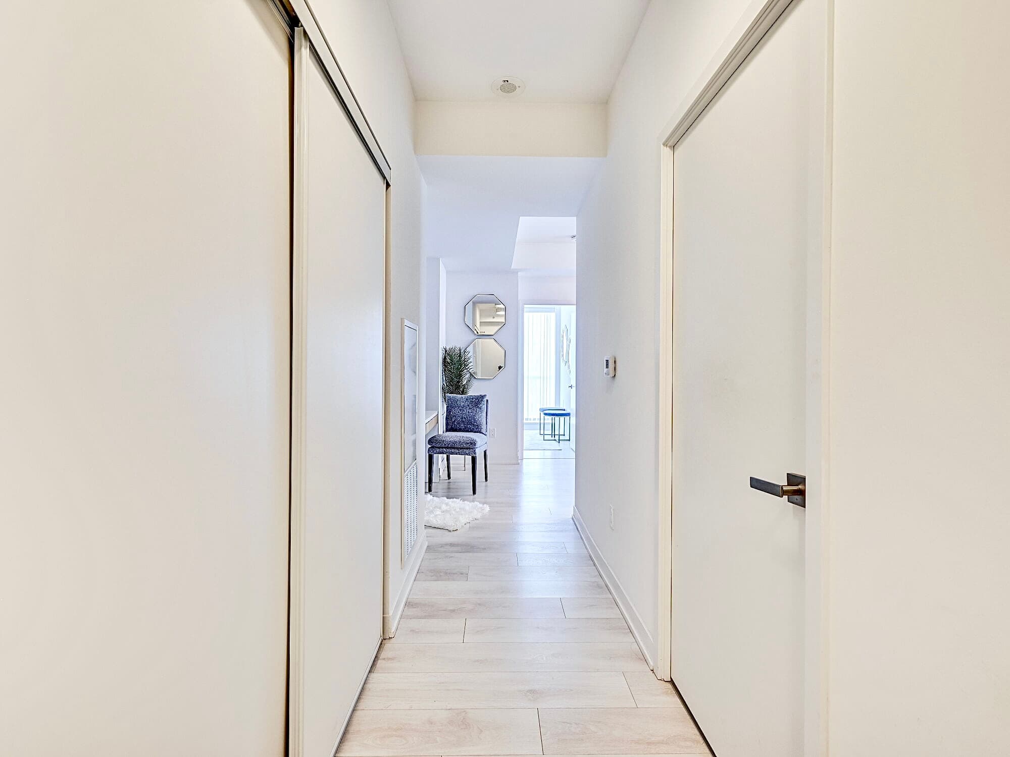 Bright white hallway with light wood floors leading to a room with a blue chair.