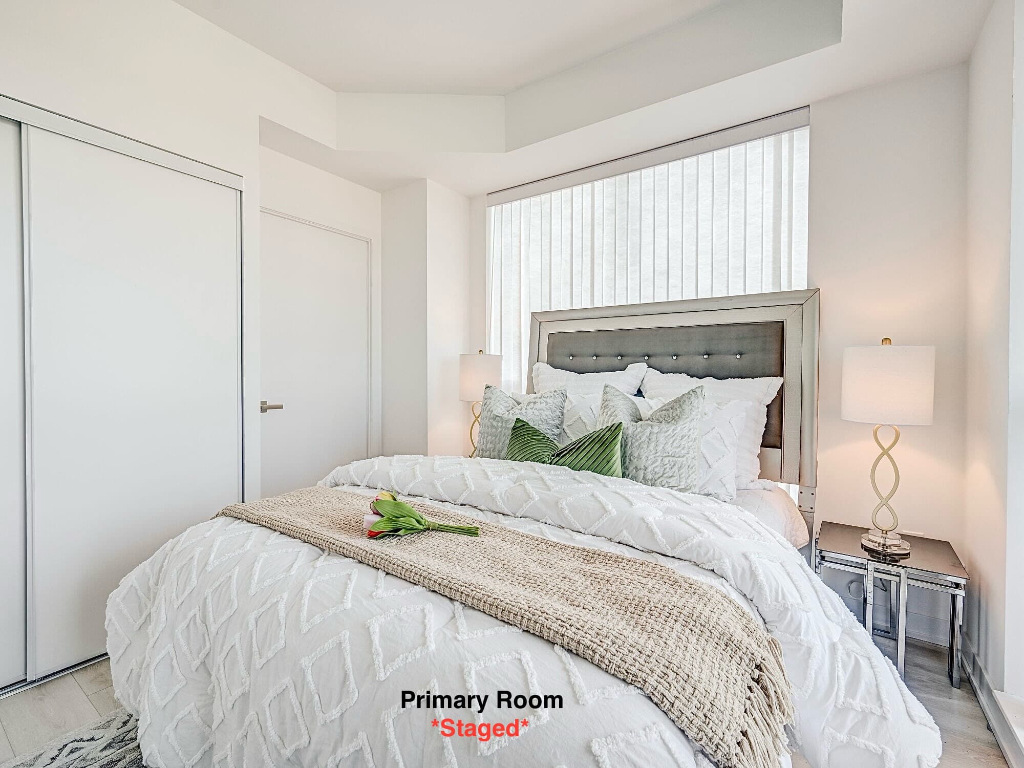 Staged primary bedroom featuring white textured bedding, grey tufted headboard, and modern bedside lamps.