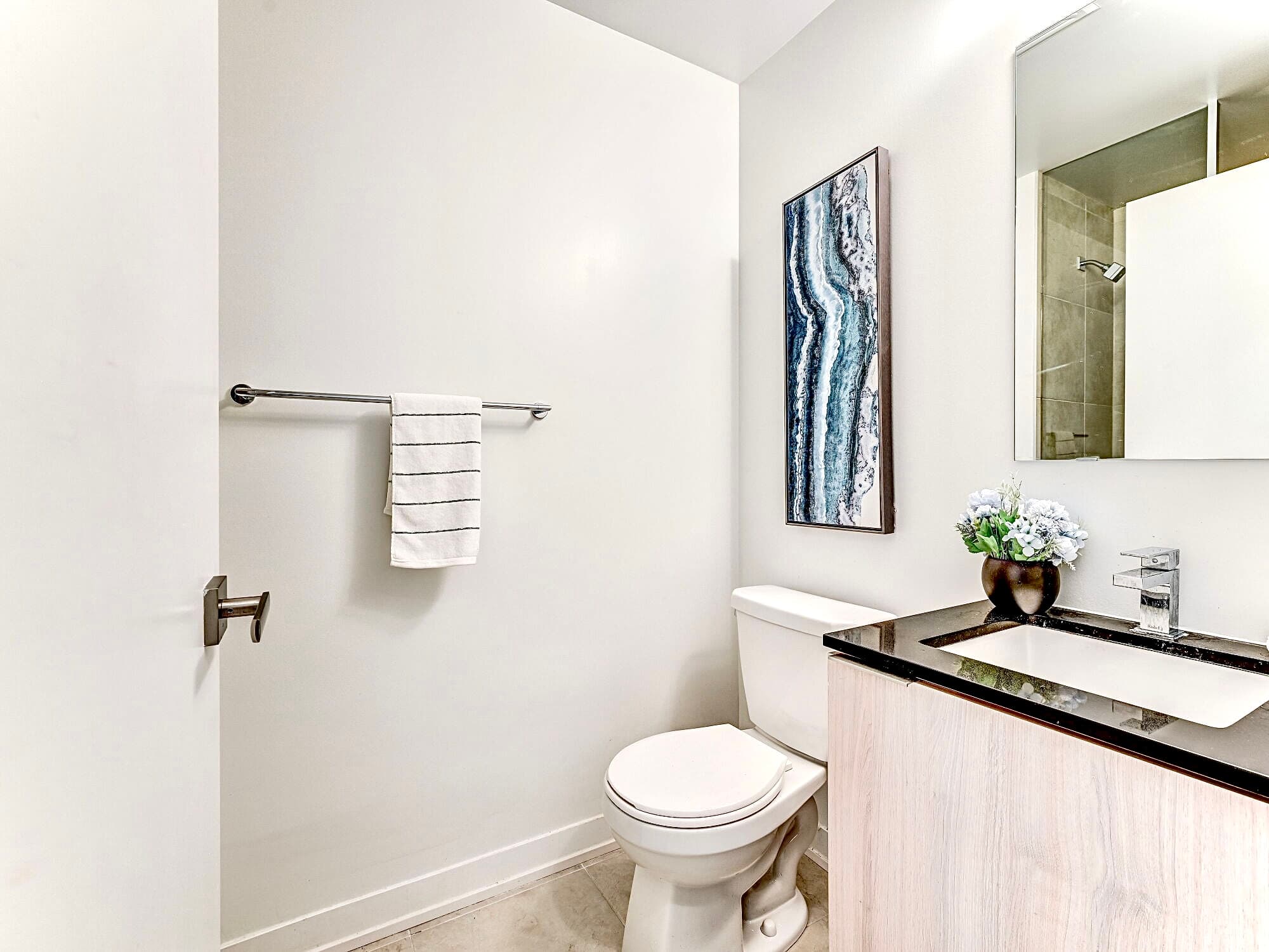 Bright modern bathroom with a white toilet, black countertop vanity, and blue abstract wall art.