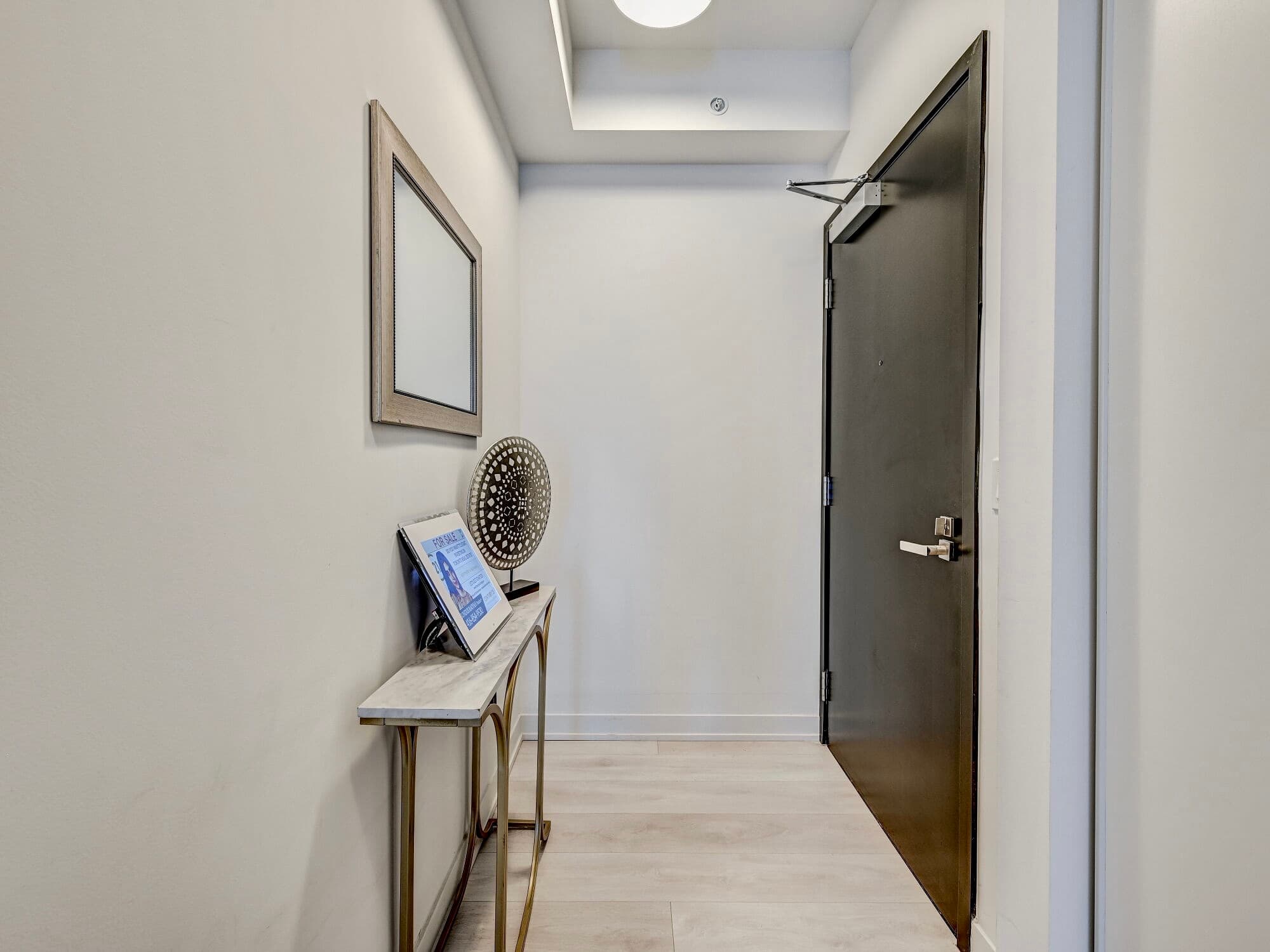 Modern entryway with a black door, marble console table, gold legs, and wall mirror.