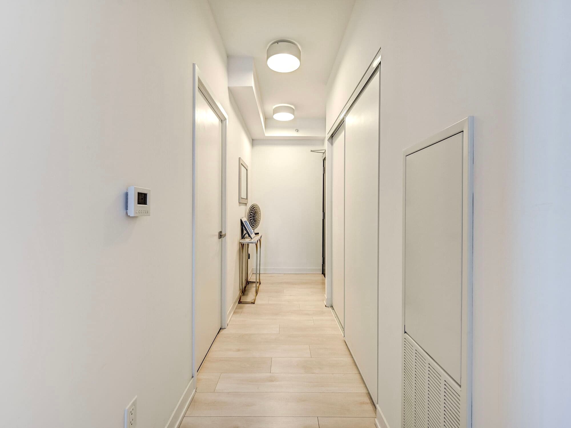 Bright white hallway with light wood floors, round ceiling lights, and white closet doors.