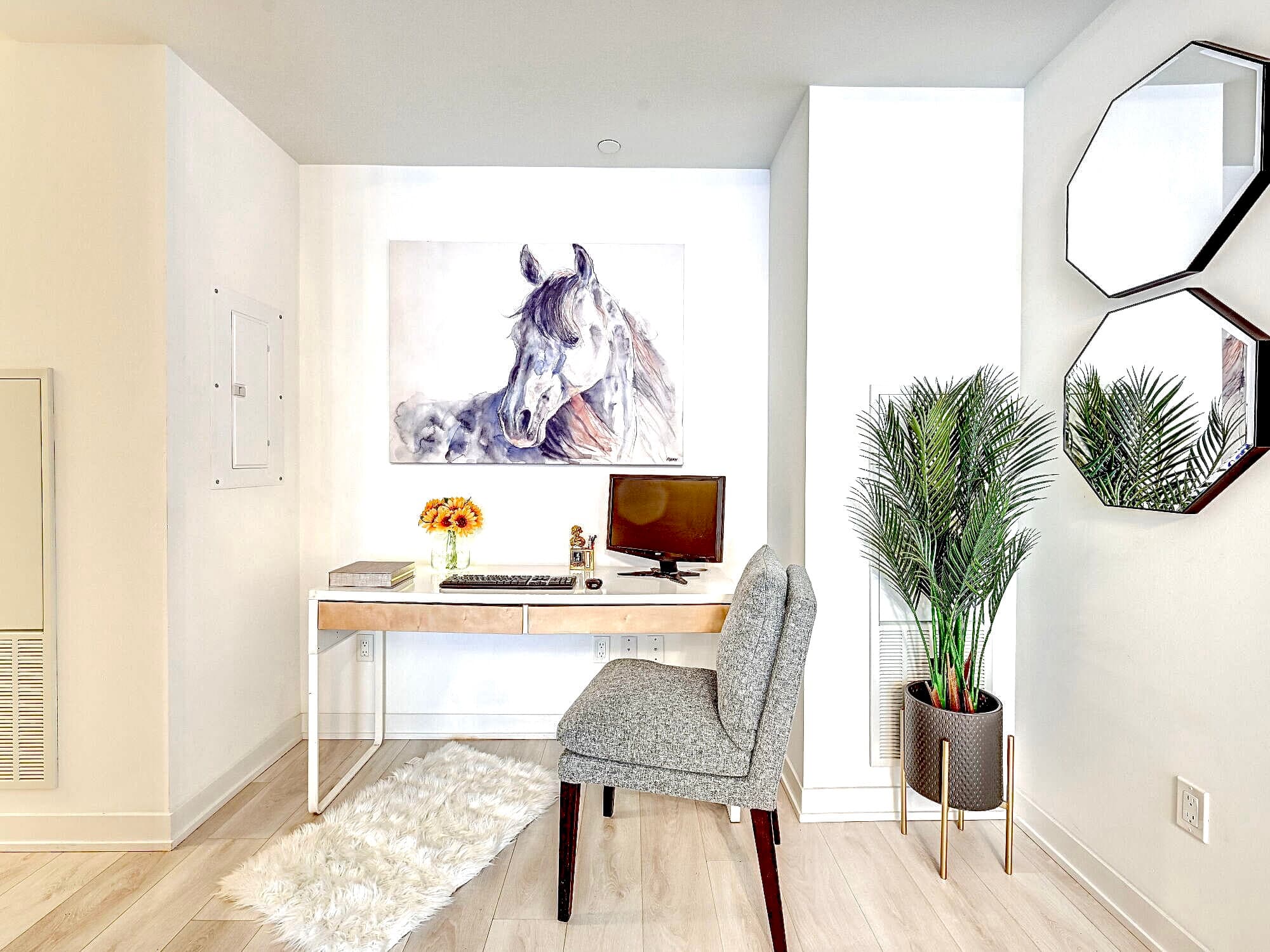Modern home office featuring a white desk, grey chair, horse painting, and potted plant.
