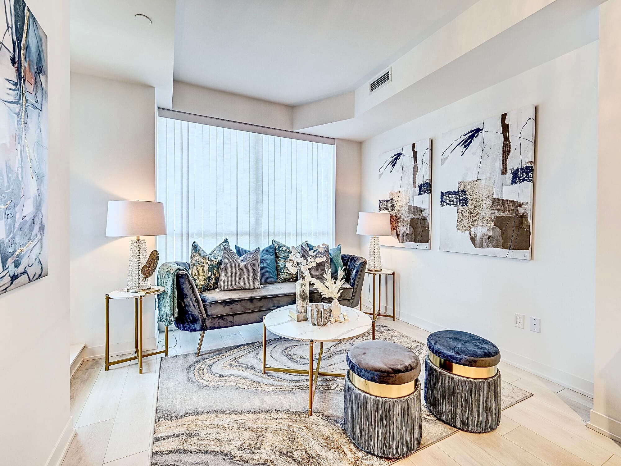 Modern living room with blue velvet sofa, marble coffee table, and large abstract wall paintings.