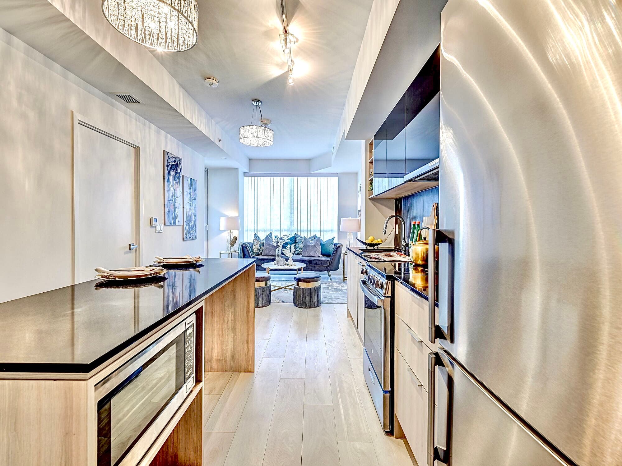 Modern kitchen with stainless steel appliances and black countertops opening into a bright living room.