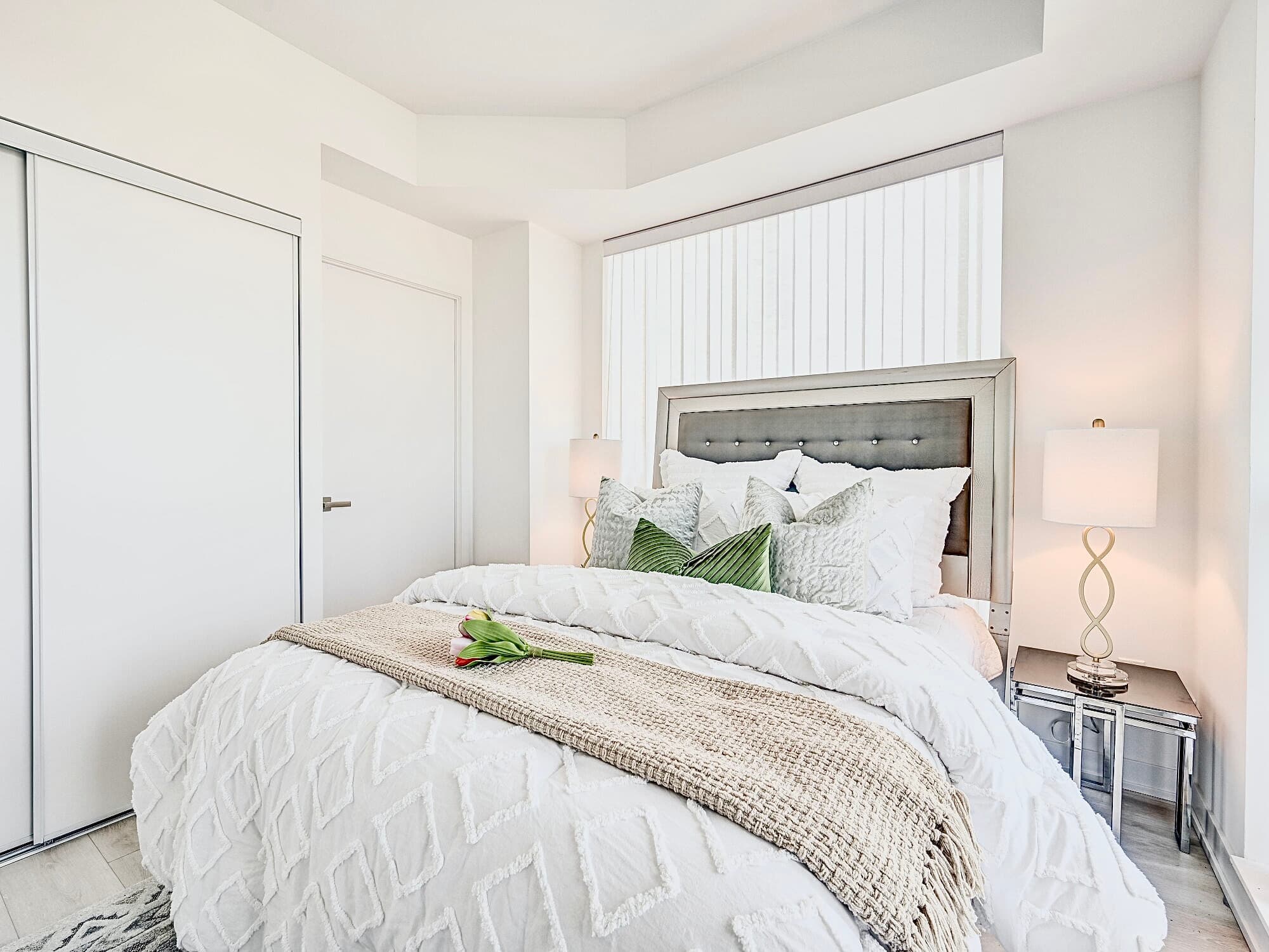 Bright modern bedroom featuring white textured bedding, a grey tufted headboard, and green pillows.
