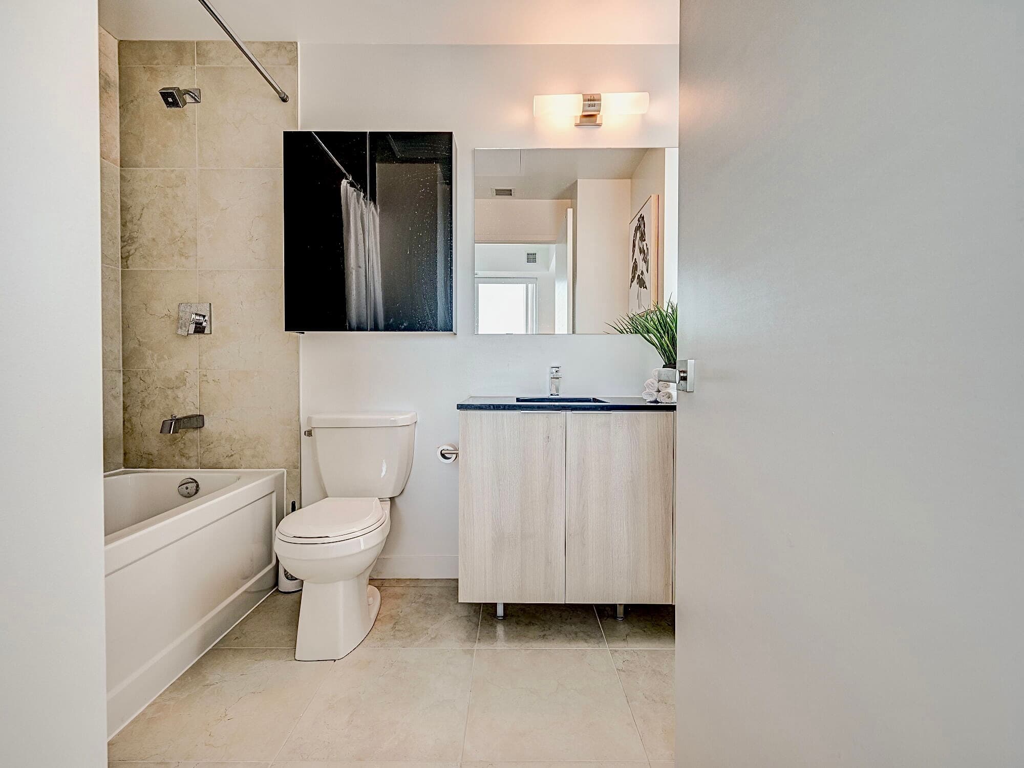 Modern bathroom featuring a white bathtub, toilet, and light wood vanity with black countertop.