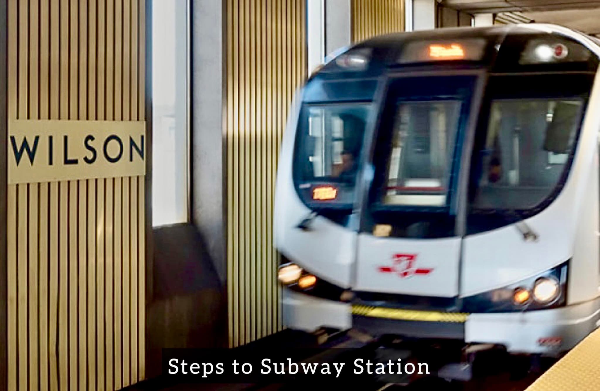 White Toronto subway train pulls into Wilson station beside a wall of vertical wooden slats.
