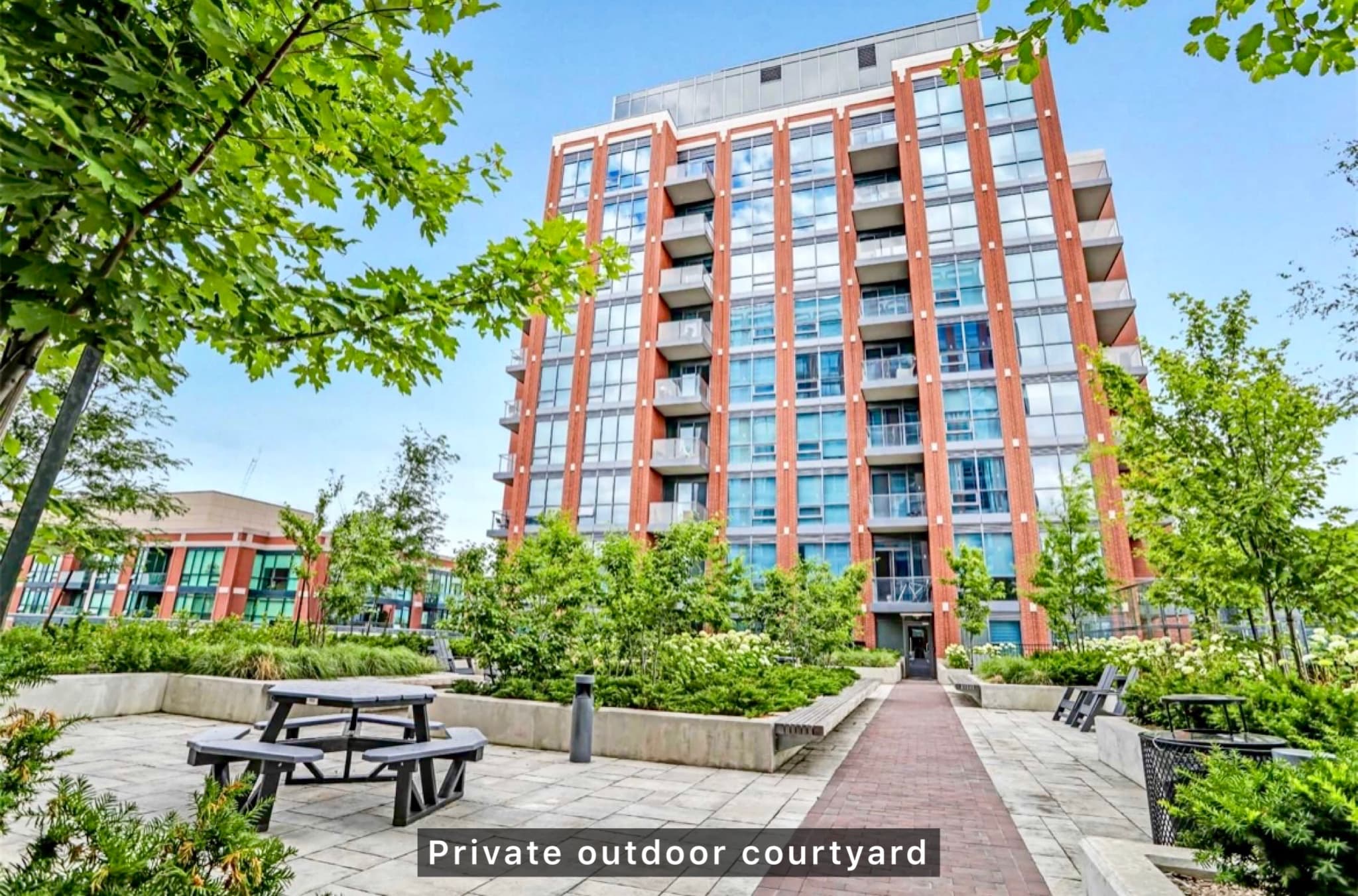Modern brick apartment building overlooking a private courtyard with lush greenery and outdoor seating.