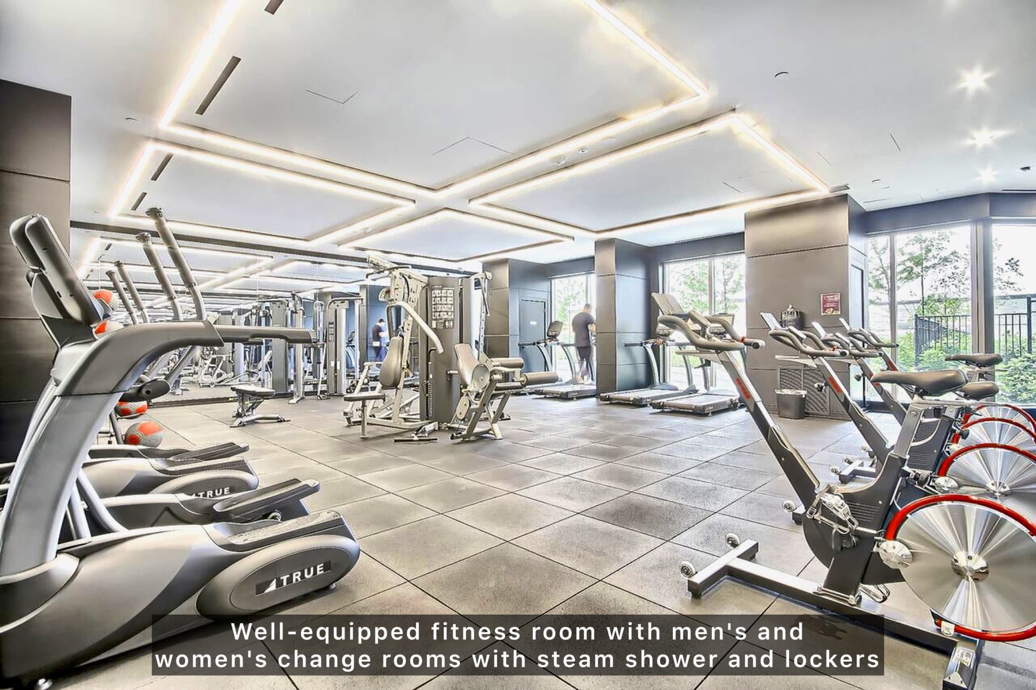 Modern fitness room with ellipticals, stationary bikes, and treadmills under bright rectangular ceiling lights.