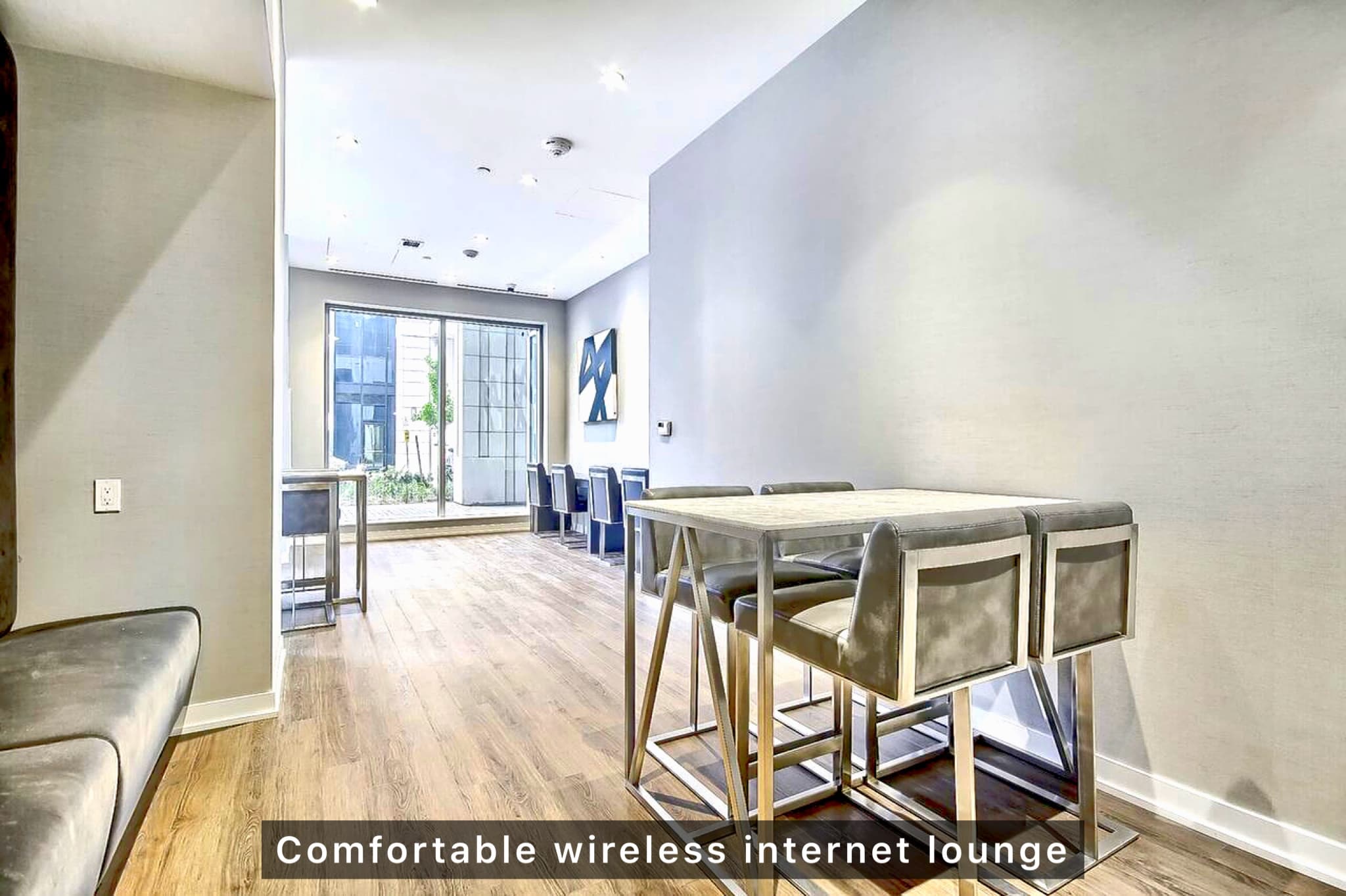 Modern lounge with high-top tables, grey upholstered chairs, wood flooring, and large windows.